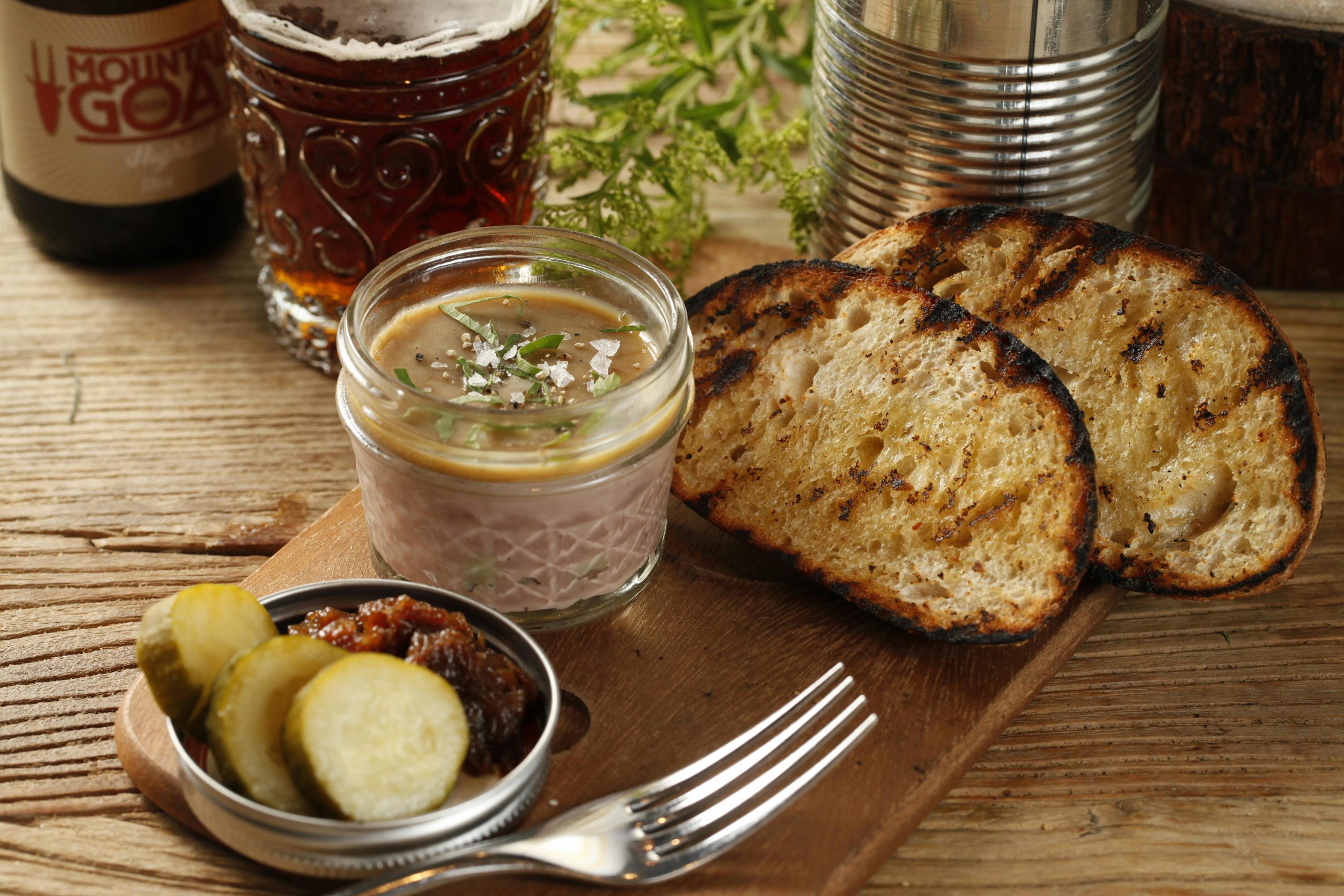 Delicious pate served with pickles and grilled bread on a wooden table, perfect for food enthusiasts.
